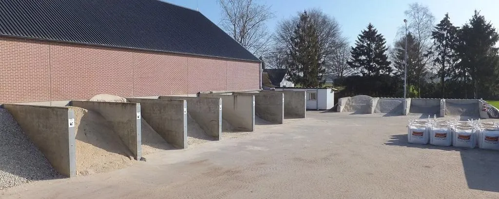 Betonnen opslagvakken met hopen zand en grind voor een bakstenen loods, rechts witte big bags