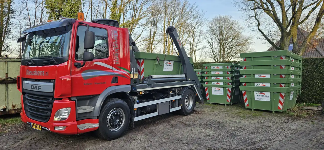 Rode DAF-portaalarmwagen van Kleuskens met een groene container, rechts gestapelde groene portaalarmcontainers